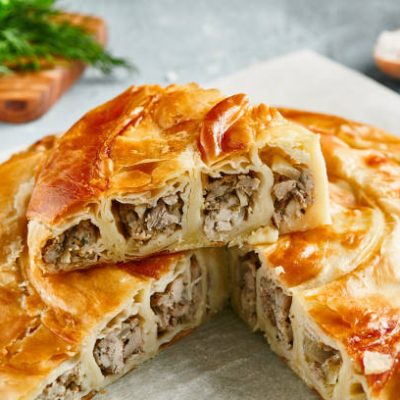 Classic turkish pie with meat on wooden board. Composition with burek pie on concrete background with textile and spices. Balkan pie with minced meat  in rustic style on gray table